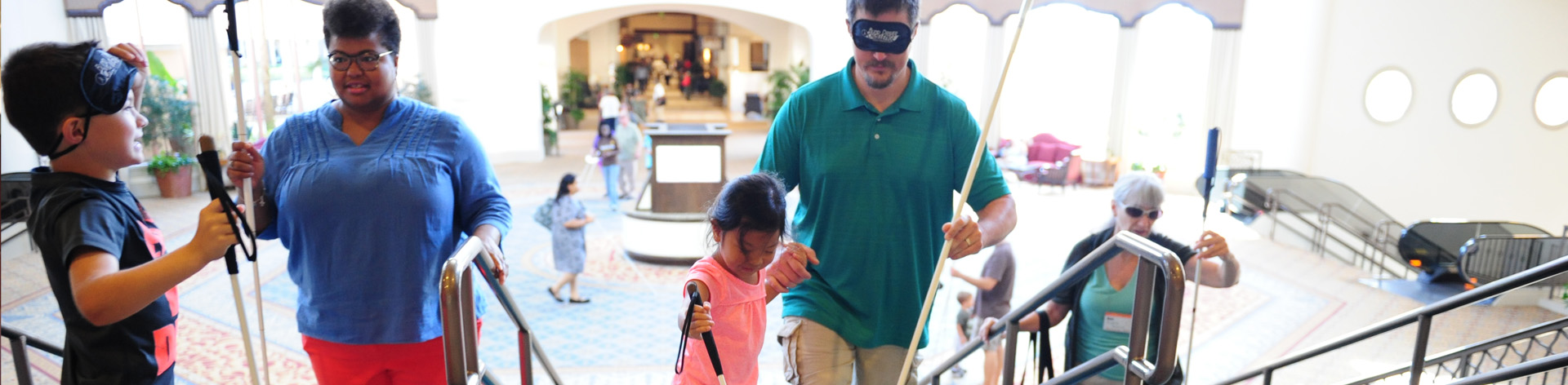 During and O&M training a blind child leads her father up the stairs with her long white cane. Her father wears sleepshades and also uses a cane.